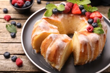 Pieces of delicious bundt cake with berries, glaze and mint on wooden table, closeup