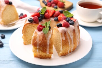 Pieces of delicious bundt cake with berries, glaze and mint on light blue wooden table, closeup