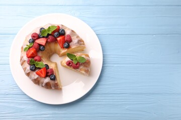 Pieces of delicious bundt cake with berries, glaze and mint on light blue wooden table, top view. Space for text