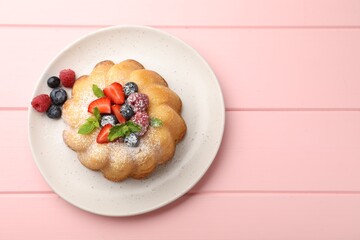 Delicious bundt cake with powdered sugar, berries and mint on pink wooden table, top view. Space for text