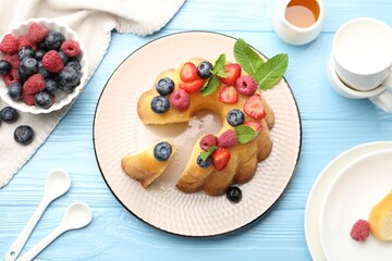Tasty Bundt cake with berries, honey and mint on light blue wooden table, flat lay
