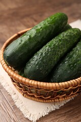 Fresh cucumbers in wicker basket on wooden table, closeup