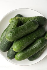 Fresh cucumbers in bowl on white table, top view
