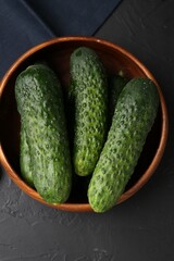 Fresh cucumbers in bowl on dark textured table, top view