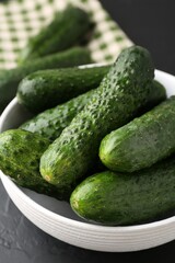 Fresh cucumbers in bowl on dark textured table, closeup