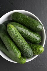 Fresh cucumbers in bowl on dark textured table, top view