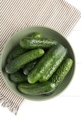 Fresh cucumbers in bowl on white wooden table, top view