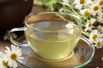 Tasty chamomile tea and flowers on wooden table, closeup