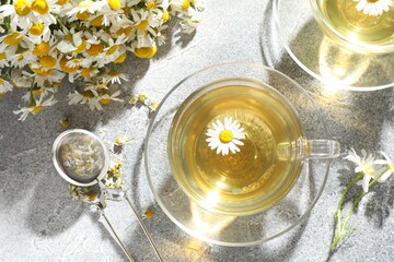 Tasty chamomile tea, infuser and flowers on light grey table, flat lay
