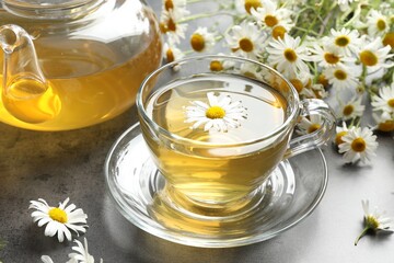 Tasty chamomile tea and flowers on grey table, closeup
