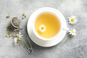Tasty chamomile tea, infuser and flowers on light grey table, flat lay