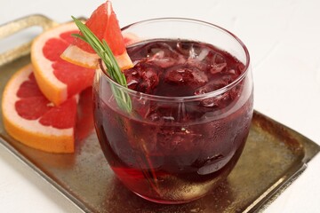Tasty cocktail with grapefruit, ice cubes and rosemary on white table, closeup