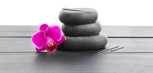 Acupuncture needles, orchid flower and stack of spa stones on grey wooden table against white...