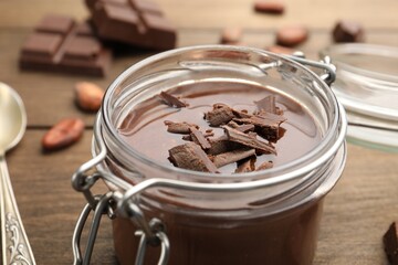 Delicious chocolate panna cotta in glass jar, nuts and spoon on wooden table, closeup