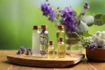 Bottles of essential oils and different plants on wooden table outdoors, closeup