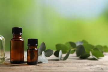 Bottles of essential oils and eucalyptus branch on wooden table outdoors, closeup