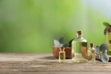 Bottles of essential oils and eucalyptus leaves on wooden table outdoors, space for text