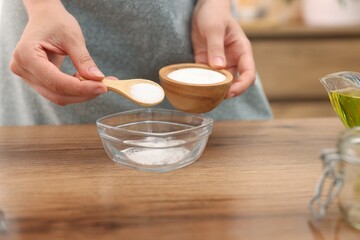 Making natural scrub. Woman adding sugar into bowl at wooden table, closeup