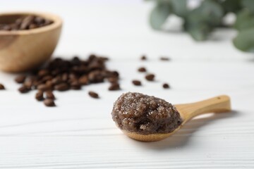 Natural body scrub in spoon, coffee beans and eucalyptus on white wooden table, closeup. Space for...