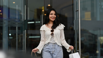 Confident shopper enjoying a successful day out, smiling and holding to her bags in an urban setting