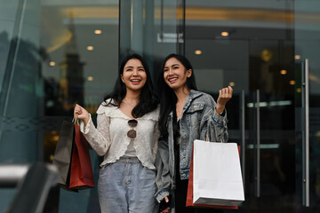 Two best friends standing outside a mall, holding shopping bags and smiling with excitement, Urban lifestyle moment concept