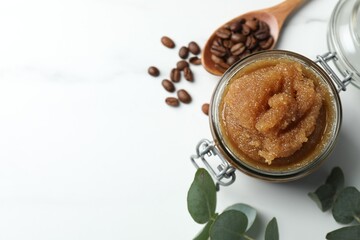 Natural body scrub, coffee beans and eucalyptus leaves on white table, flat lay. Space for text