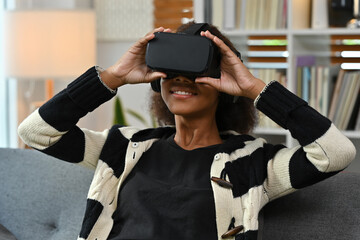 Happy African girl wearing a VR headset, immersed in interactive entertainment in a cozy modern living room