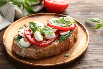 Delicious sandwich with mozzarella cheese, tomatoes and basil on wooden table, closeup