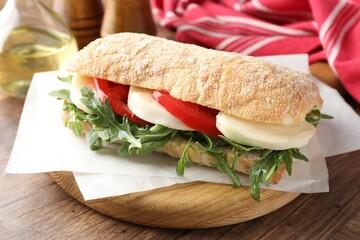 Delicious sandwich with mozzarella cheese, tomato and arugula on wooden table, closeup