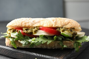Delicious sandwich with mozzarella cheese, pesto, tomato and arugula on table, closeup