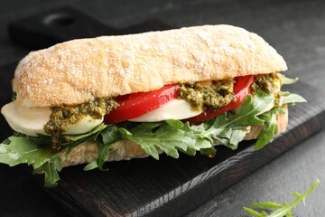 Delicious sandwich with mozzarella cheese, pesto, tomato and arugula on black table, closeup