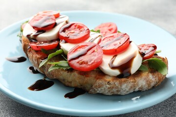 Delicious sandwich with mozzarella cheese, balsamic sauce, tomato and arugula on grey table, closeup