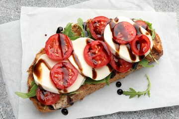 Delicious sandwich with mozzarella cheese, balsamic sauce, tomato and arugula on grey table, top view