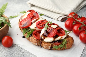 Delicious sandwich with mozzarella cheese, balsamic sauce, tomatoes and arugula on grey table, closeup