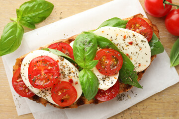 Delicious sandwich with mozzarella cheese, tomatoes and basil on wooden table, flat lay
