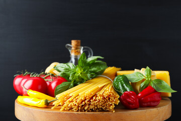 Raw spaghetti pasta and products on wooden board against black background, closeup
