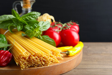 Raw spaghetti pasta and products on wooden table against black background, closeup