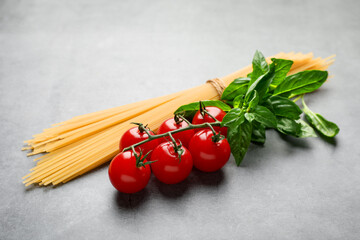 Raw spaghetti pasta, tomatoes and basil on grey textured table, closeup