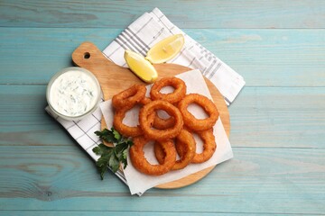Fried squid rings served with sauce on light blue wooden table, flat lay
