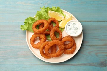 Fried squid rings served with sauce on light blue wooden table, top view