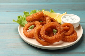 Fried squid rings served with sauce on light blue wooden table, closeup