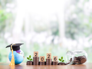 Earth globe with graduation hat, Wooden block with number 2026 and plant growing on stack of coins....