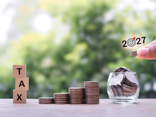 Hand putting coin into glass bottle, Wooden blocks with the word TAX and stack of coins. The...