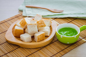 Slice steamed bread on wooden plate and pandan custard in bowl