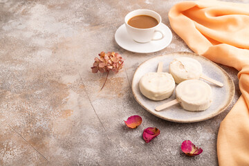 Сhocolate Ice cream in white glaze, cup of coffee, on brown concrete and orange textile, side view, copy space