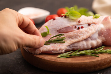 Raw Turkey Thigh with spices on cutting board on black concrete with hand, linen textile. side view, close up, selective focus