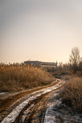 A quiet rural dirt road covered in a thin layer of snow, leading through dry grass fields towards...