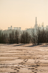 A winter landscape with footprints in the snow-covered field, leading towards a distant industrial...