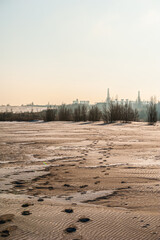 A winter landscape with footprints in the snow-covered field, leading towards a distant industrial...