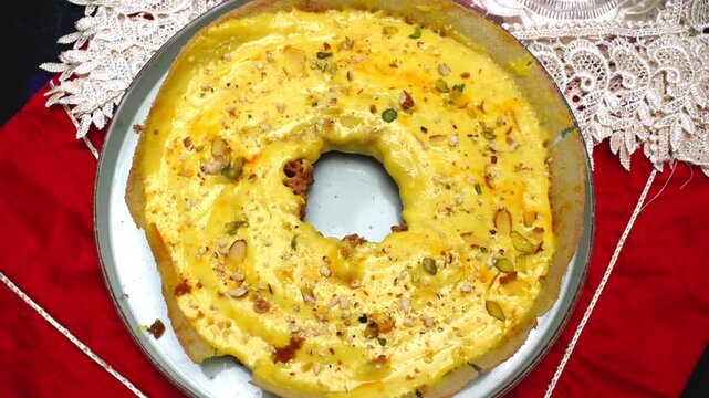 Video clip of Traditional Rajasthani Malai Ghevar Dessert made with flour, ghee, sugar syrup, and topped with creamy malai and dry fruits. Popular Indian sweet enjoyed during Teej, Diwali and winter. 